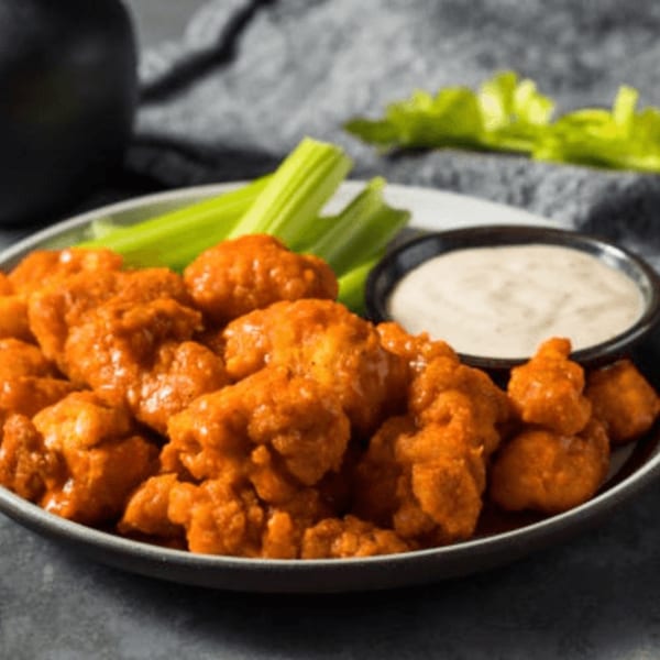 A plate of Flicks' buffalo cauliflower bites with celery sticks and a side of ranch dressing.