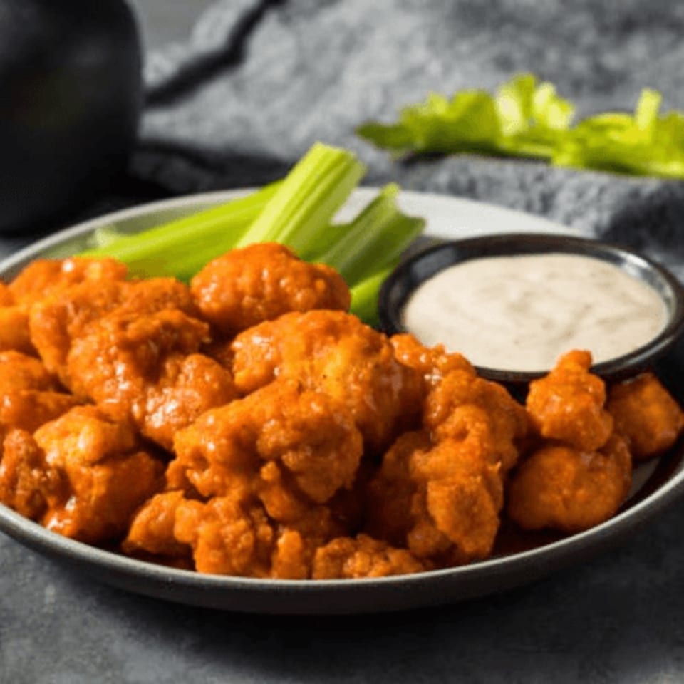 A plate of Flicks' buffalo cauliflower bites with celery sticks and a side of ranch dressing.